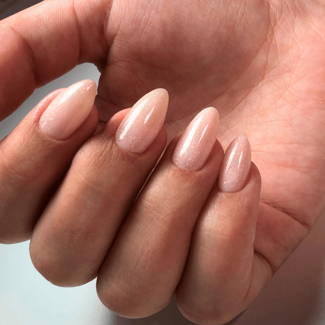 Womans hand with almond acrylic nude nails with light silver shimmer