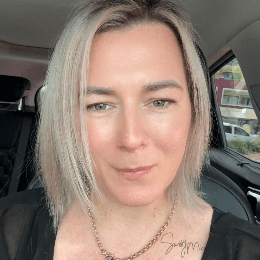 Carly Wallace, owner of Sassy Minx, smiling in her car wearing a black top and gold chain.